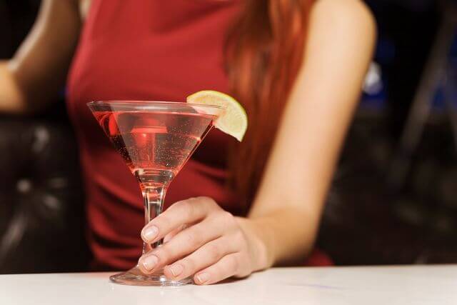 赤いカクテルを持っている赤いドレスの女性の胸元